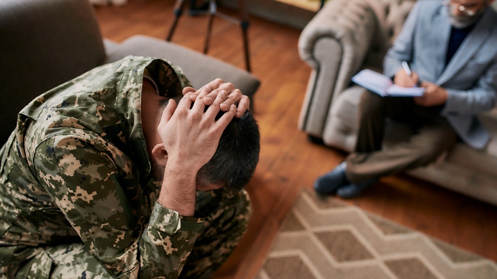 Middle aged military man holding his head in pain and depression during therapy session