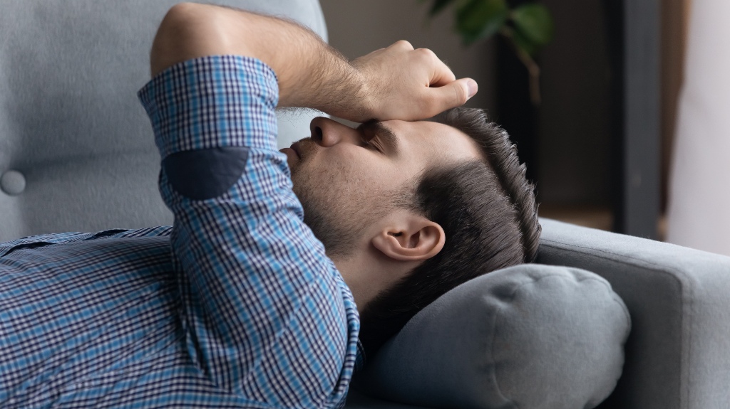 Tired frustrated millennial man lying on sofa at home