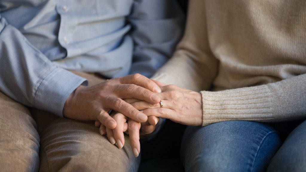 Senior family couple sitting on sofa, holding hands
